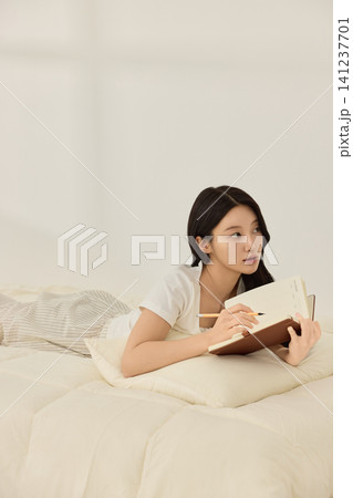 Woman writing in a notebook on a bright bedroom bed 141237701