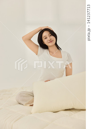 Woman sitting on a cream bed during a calm morning routine 141237713