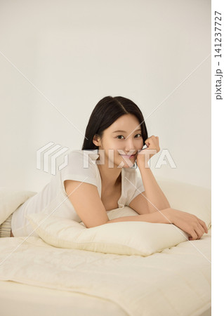 Young Asian woman smiling on a bed with an alarm clock Young Asian woman smiling on a bed with an alarm clock 141237727
