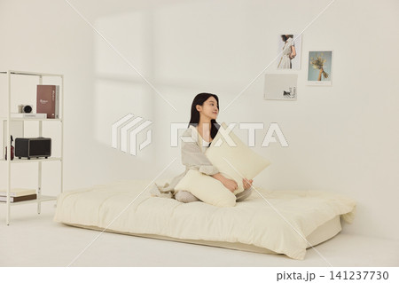 Young Asian woman stretching on a cream bed in a bright bedroom 141237730