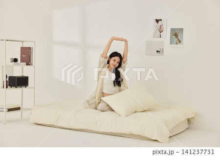 Woman sitting on a bed with pillows during a morning routine Woman sitting on a bed with pillows during a morning routine 141237731