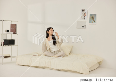 Woman sitting on a bed with pillows during a morning routine 141237748