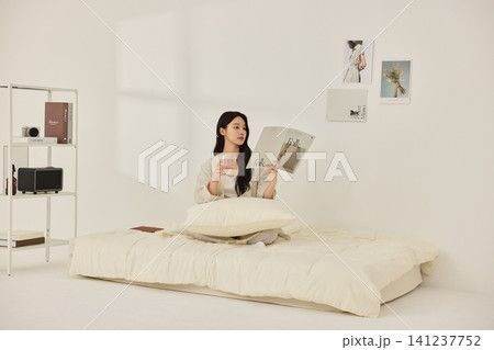 Young Asian woman stretching on a cream bed in a bright bedroom Young Asian woman stretching on a cream bed in a bright bedroom 141237752