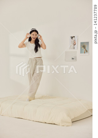 Woman stretching with a pillow in a bright minimal bedroom Woman stretching with a pillow in a bright minimal bedroom 141237789