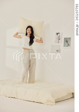 Woman stretching with a pillow in a bright minimal bedroom Woman stretching with a pillow in a bright minimal bedroom 141237793