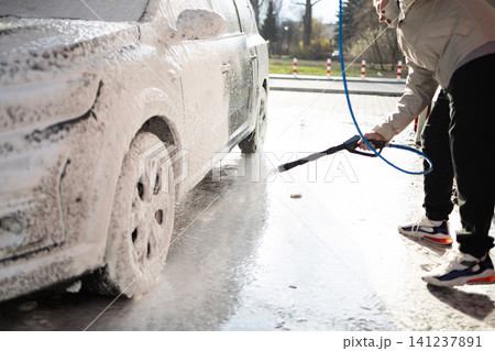 Young guy cleaning vehicle with pressure washer jet spray at manual car wash station. Young guy cleaning vehicle with pressure washer jet spray at manual car wash station. 141237891