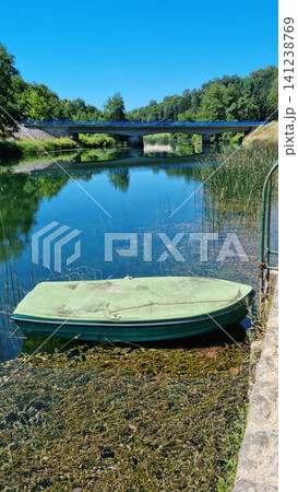 Small green boat anchored on the Dobra river in Jarce Polje 141238769