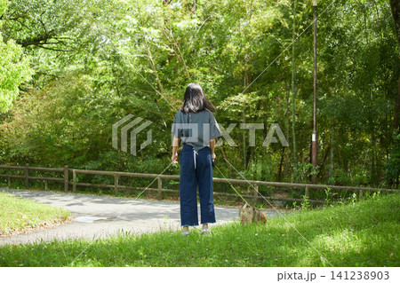 春の公園で可愛いポメラニアンの子犬を抱っこして散歩する私服の十代の女の子の姿	 141238903