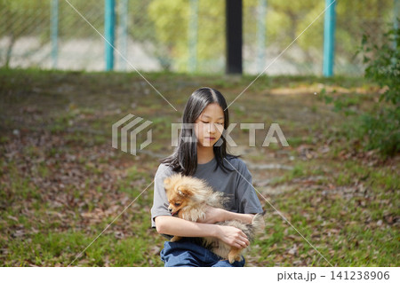 春の公園で可愛いポメラニアンの子犬を抱っこして散歩する私服の十代の女の子の姿 春の公園で可愛いポメラニアンの子犬を抱っこして散歩する私服の十代の女の子の姿 141238906