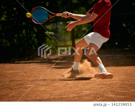 Tennis player sliding with backhand on clay court with dust and racket detail. Tennis player sliding with backhand on clay court with dust and racket detail. 141239053