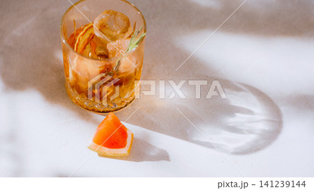 Amber grapefruit cocktail with rosemary, ice and large sunlight shadow copy space. Amber grapefruit cocktail with rosemary, ice and large sunlight shadow copy space. 141239144