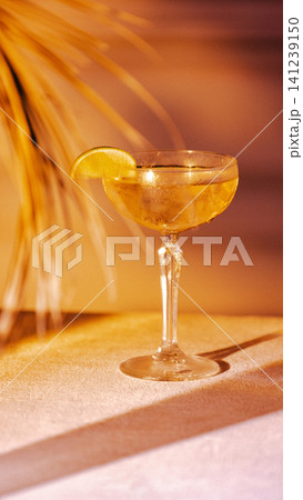 Golden coupe cocktail with lime garnish and warm evening bar atmosphere. Golden coupe cocktail with lime garnish and warm evening bar atmosphere. 141239150
