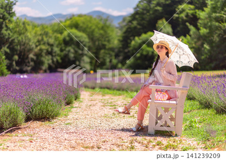 Graceful Caucasian woman sitting on bench in vibrant lavender field during Provence vacation. Natural beauty and elegance define relaxed summer lifestyle. Graceful Caucasian woman sitting on bench in vibrant lavender field during Provence vacation. Natural beauty and elegance define relaxed summer lifestyle. 141239209
