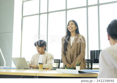 Young cheerful Asian business woman discussing project with colleagues while working together in the modern office. Young cheerful Asian business woman discussing project with colleagues while working together in the modern office. 141239648
