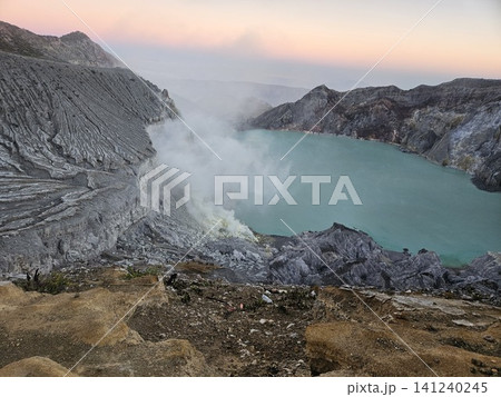 The stunning panoramic sunrise view of the turquoise acid crater lake at Mount Ijen volcano, featuring majestic rocky mountain ridges and thick sulfur smoke rising from the active vents in East Java. The stunning panoramic sunrise view of the turquoise acid crater lake at Mount Ijen volcano, featuring majestic rocky mountain ridges and thick sulfur smoke rising from the active vents in East Java. 141240245