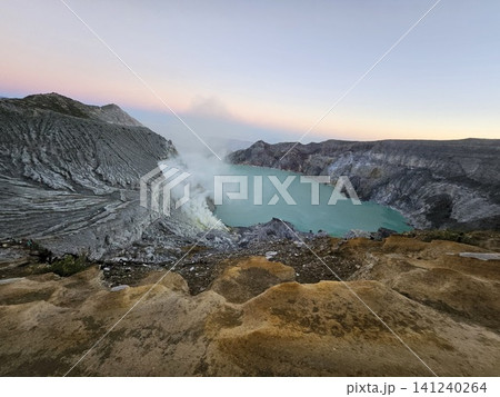 The stunning panoramic sunrise view of the turquoise acid crater lake at Mount Ijen volcano, featuring majestic rocky mountain ridges and thick sulfur smoke rising from the active vents in East Java. The stunning panoramic sunrise view of the turquoise acid crater lake at Mount Ijen volcano, featuring majestic rocky mountain ridges and thick sulfur smoke rising from the active vents in East Java. 141240264