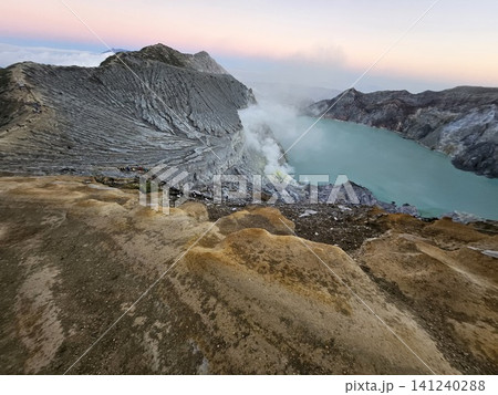 The stunning panoramic sunrise view of the turquoise acid crater lake at Mount Ijen volcano, featuring majestic rocky mountain ridges and thick sulfur smoke rising from the active vents in East Java. The stunning panoramic sunrise view of the turquoise acid crater lake at Mount Ijen volcano, featuring majestic rocky mountain ridges and thick sulfur smoke rising from the active vents in East Java. 141240288