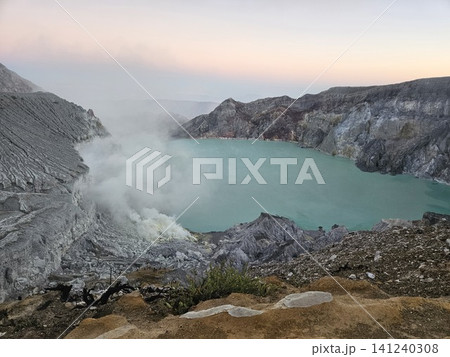 The stunning panoramic sunrise view of the turquoise acid crater lake at Mount Ijen volcano, featuring majestic rocky mountain ridges and thick sulfur smoke rising from the active vents in East Java. The stunning panoramic sunrise view of the turquoise acid crater lake at Mount Ijen volcano, featuring majestic rocky mountain ridges and thick sulfur smoke rising from the active vents in East Java. 141240308