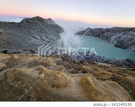 The stunning panoramic sunrise view of the turquoise acid crater lake at Mount Ijen volcano, featuring majestic rocky mountain ridges and thick sulfur smoke rising from the active vents in East Java. The stunning panoramic sunrise view of the turquoise acid crater lake at Mount Ijen volcano, featuring majestic rocky mountain ridges and thick sulfur smoke rising from the active vents in East Java. 141240330