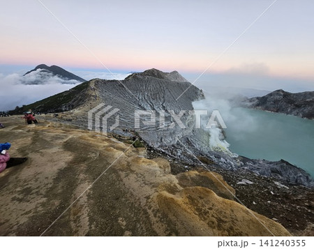 The stunning panoramic sunrise view of the turquoise acid crater lake at Mount Ijen volcano, featuring majestic rocky mountain ridges and thick sulfur smoke rising from the active vents in East Java. The stunning panoramic sunrise view of the turquoise acid crater lake at Mount Ijen volcano, featuring majestic rocky mountain ridges and thick sulfur smoke rising from the active vents in East Java. 141240355