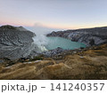 The stunning panoramic sunrise view of the turquoise acid crater lake at Mount Ijen volcano, featuring majestic rocky mountain ridges and thick sulfur smoke rising from the active vents in East Java. 141240357