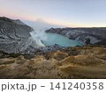 The stunning panoramic sunrise view of the turquoise acid crater lake at Mount Ijen volcano, featuring majestic rocky mountain ridges and thick sulfur smoke rising from the active vents in East Java. 141240358