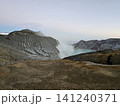 The stunning panoramic sunrise view of the turquoise acid crater lake at Mount Ijen volcano, featuring majestic rocky mountain ridges and thick sulfur smoke rising from the active vents in East Java. 141240371