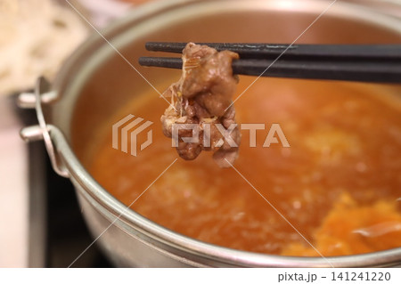 Chopsticks Holding Meat Over Hot Pot Soup 141241220