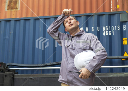 American engineer in uniform holding hard hat standing in containers yard, worker tired of frustration. American engineer in uniform holding hard hat standing in containers yard, worker tired of frustration. 141242049