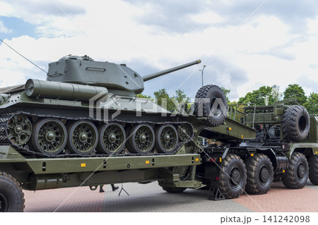Side profile view of a vintage historic Soviet tank loaded onto a modern heavy-duty multi-axle tank transporter trailer. Side profile view of a vintage historic Soviet tank loaded onto a modern heavy-duty multi-axle tank transporter trailer. 141242098