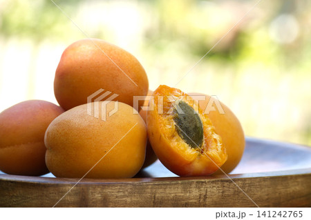 Fresh ripe apricots piled in a wooden bowl with one cut in half showing the pit 141242765