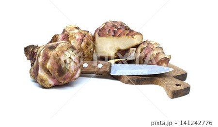 Jerusalem artichokes with a knife on a wooden cutting board against a white background 141242776