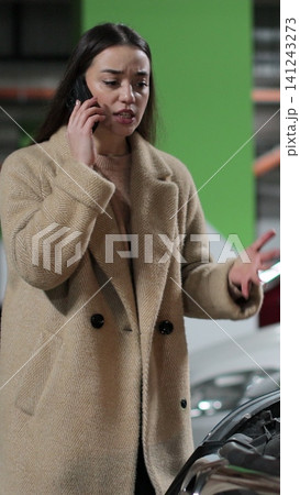 Vertical video Desperate woman stands by a broken car in the parking lot of shopping cent and calls the car service. Problems with the car. Vertical video Desperate woman stands by a broken car in the parking lot of shopping cent and calls the car service. Problems with the car. 141243273