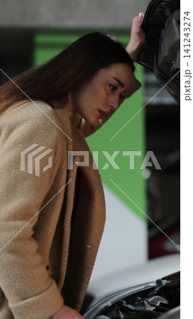 Vertical video Young woman driver near broken car with popped hood having a breakdown problem with her vehicle. 141243274