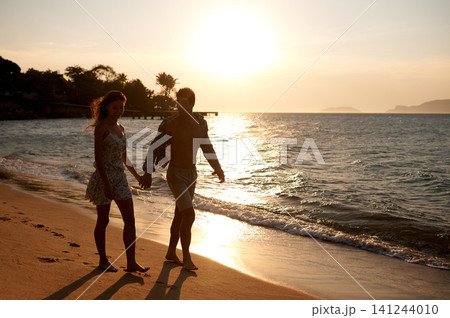Love, sunset sky and couple walking at ocean for tropical holiday adventure, relax and bonding together. Nature, man and woman on romantic date with beach, island and evening waves on happy vacation. Love, sunset sky and couple walking at ocean for tropical holiday adventure, relax and bonding together. Nature, man and woman on romantic date with beach, island and evening waves on happy vacation. 141244010
