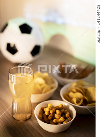 Assorted snacks, beverage and a soccer ball on a table for a football match viewing, illustrating a social sports evening. Assorted snacks, beverage and a soccer ball on a table for a football match viewing, illustrating a social sports evening. 141244428