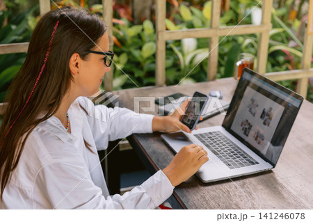 Woman working remotely with laptop and smartphone outdoors in tropical garden setting Woman working remotely with laptop and smartphone outdoors in tropical garden setting 141246078