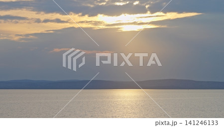 Sun setting over calm lake water and distant mountains Sun setting over calm lake water and distant mountains 141246133