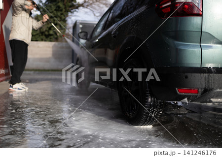 Young guy cleaning modern crossover vehicle with pressure washer jet at manual car wash. 141246176