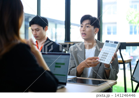 Young Asian Businessman Holding Calculator During Business Meeting with Colleagues in Modern Office Young Asian Businessman Holding Calculator During Business Meeting with Colleagues in Modern Office 141246446