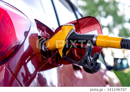 Close-Up View of a Fuel Pump Nozzle Refueling a Red Car at a Gas Station, Highlighting the Importance of Fueling and Vehicle Maintenance Close-Up View of a Fuel Pump Nozzle Refueling a Red Car at a Gas Station, Highlighting the Importance of Fueling and Vehicle Maintenance 141246787