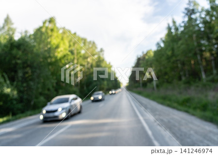 A Scenic Drive Through Lush Green Forests on a Blurred Road with Vehicles in Motion Under a Blue Sky A Scenic Drive Through Lush Green Forests on a Blurred Road with Vehicles in Motion Under a Blue Sky 141246974