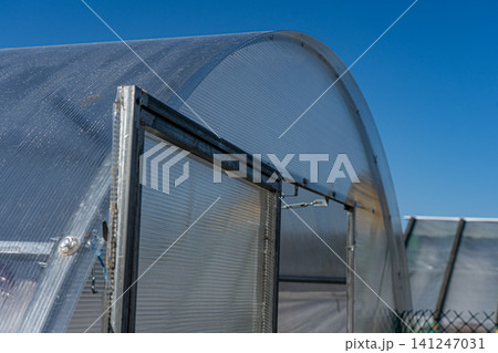 A Modern Greenhouse Structure Under a Clear Blue Sky, Showcasing Transparent Panels and an Efficient Design for Growing Plants A Modern Greenhouse Structure Under a Clear Blue Sky, Showcasing Transparent Panels and an Efficient Design for Growing Plants 141247031