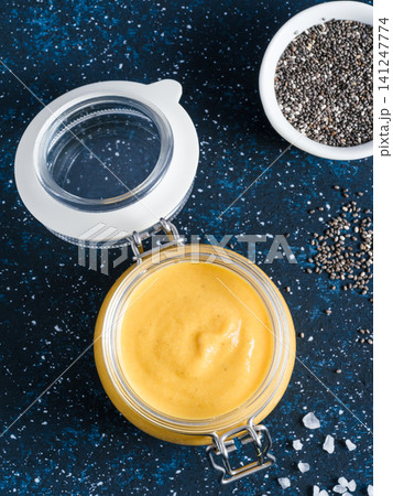 Homemade plant-based chia cheeze sauce for snacks, tacos and nachos. Creamy dairy-free dip on dark background with copy space. Vertical. Creamy Cheddar sauce with chia seeds on dark blue background 141247774