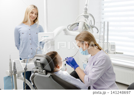 Dentist wearing mask and gloves examining young boy in dental clinic 141248697