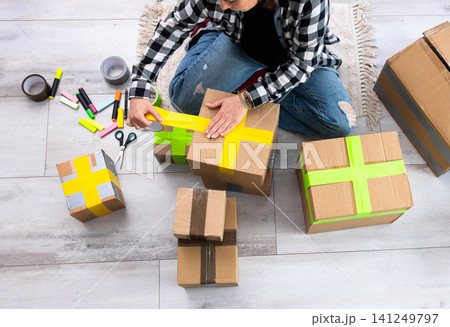 Girl Packing Cardboard Boxes And Sealing Them With Colorful Tapes 141249797
