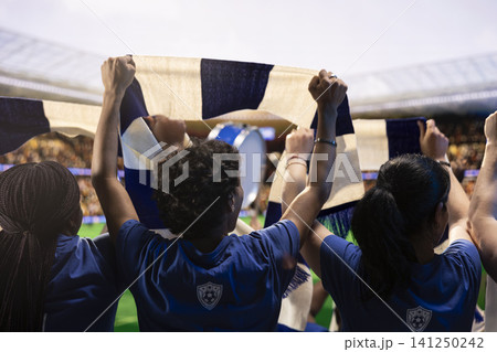 Rear view of football supporters in team jerseys raising hands and scarves during soccer match day in packed stadium. Cheering crowd creates fan chant, team support and crowd energy Rear view of football supporters in team jerseys raising hands and scarves during soccer match day in packed stadium. Cheering crowd creates fan chant, team support and crowd energy 141250242