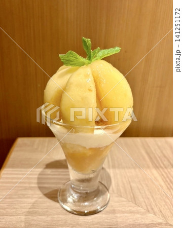 カフェの木目テーブルで楽しむ、贅沢に桃をあしらったミントがのった美味しそうな桃パフェ カフェの木目テーブルで楽しむ、贅沢に桃をあしらったミントがのった美味しそうな桃パフェ 141251172