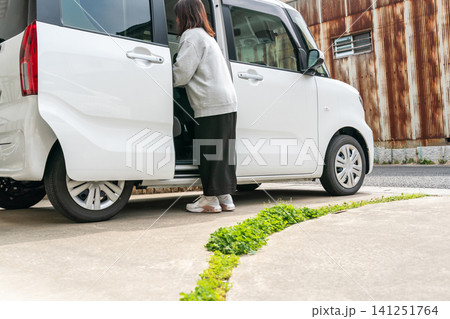 スライドドアの開いた軽自動車から荷物を下ろす主婦 スライドドアの開いた軽自動車から荷物を下ろす主婦 141251764