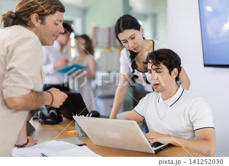 Several employees sit at desk during working day, working with laptop and paper documents. Several employees sit at desk during working day, working with laptop and paper documents. 141252030